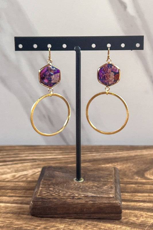 Janet Hoop Earrings - Timeless Elegance displayed on a stand, showcasing gold hoops and vibrant hexagon stone charms in purple tones.